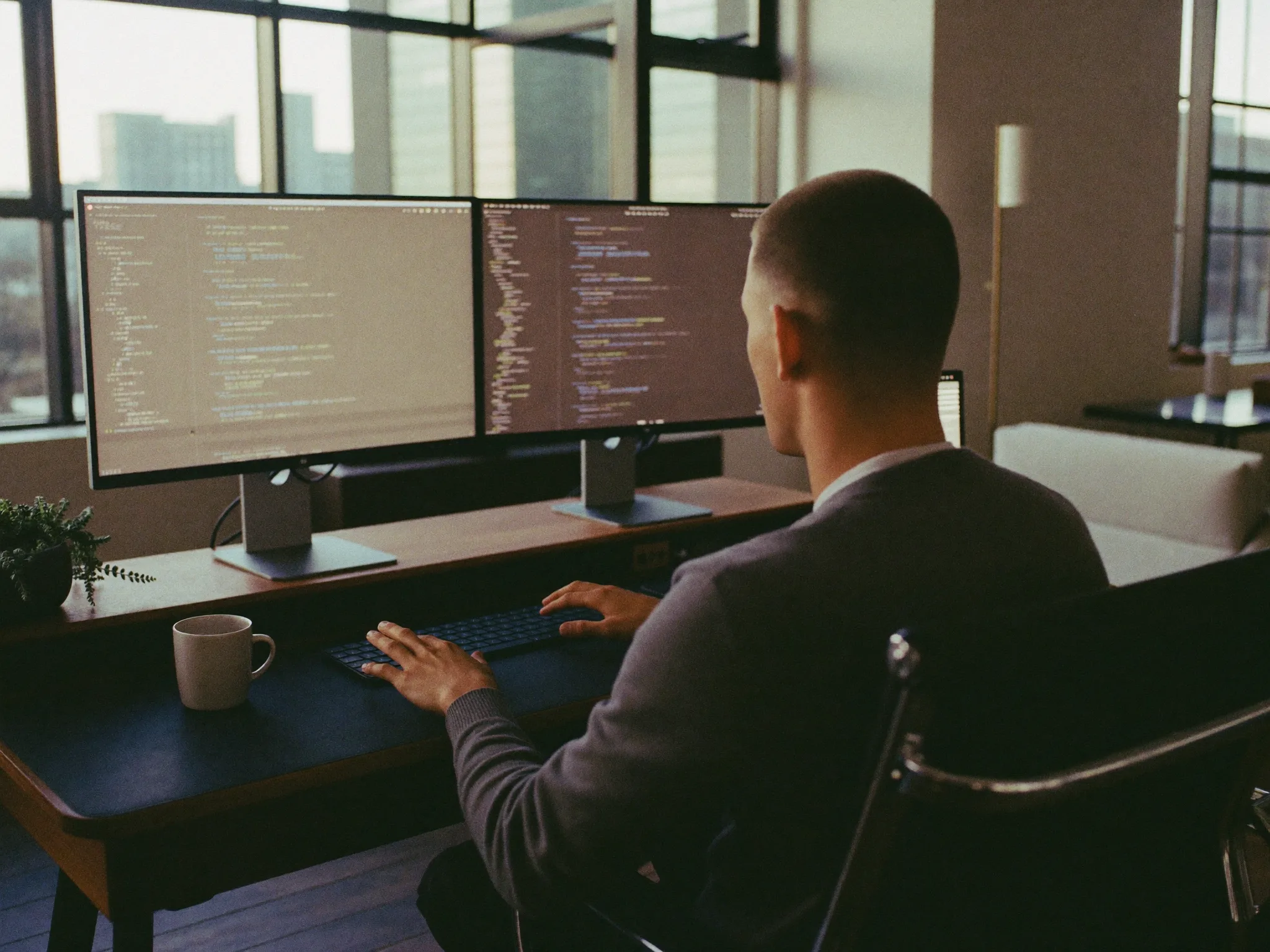 An Australian software engineer reviewing code on dual displays in a sunlit Melbourne tech studio